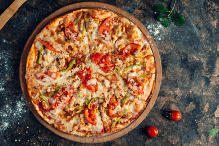 chicken pizza with bell peppers, tomato, cheese on round wooden board